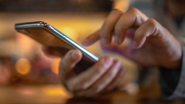 Closeup image of a man holding and using smart phone with coffee cup on wooden table in cafe 