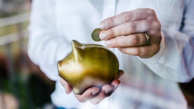 Woman putting savings in a golden piggy bank while standing in front of a window. 