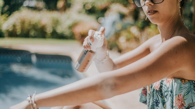 A woman spritzes her arm with spray sun screen at the pool 
