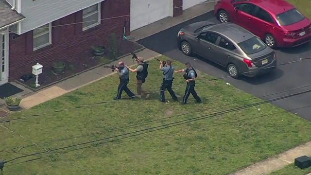 Four officers with their weapons drawn approach a home. 